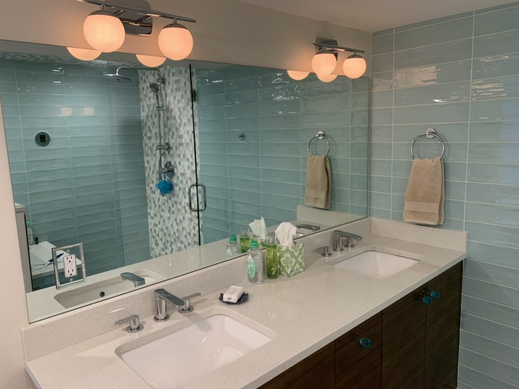 Remodeled bathroom with blue glass tile, a double vanity and a glass shower