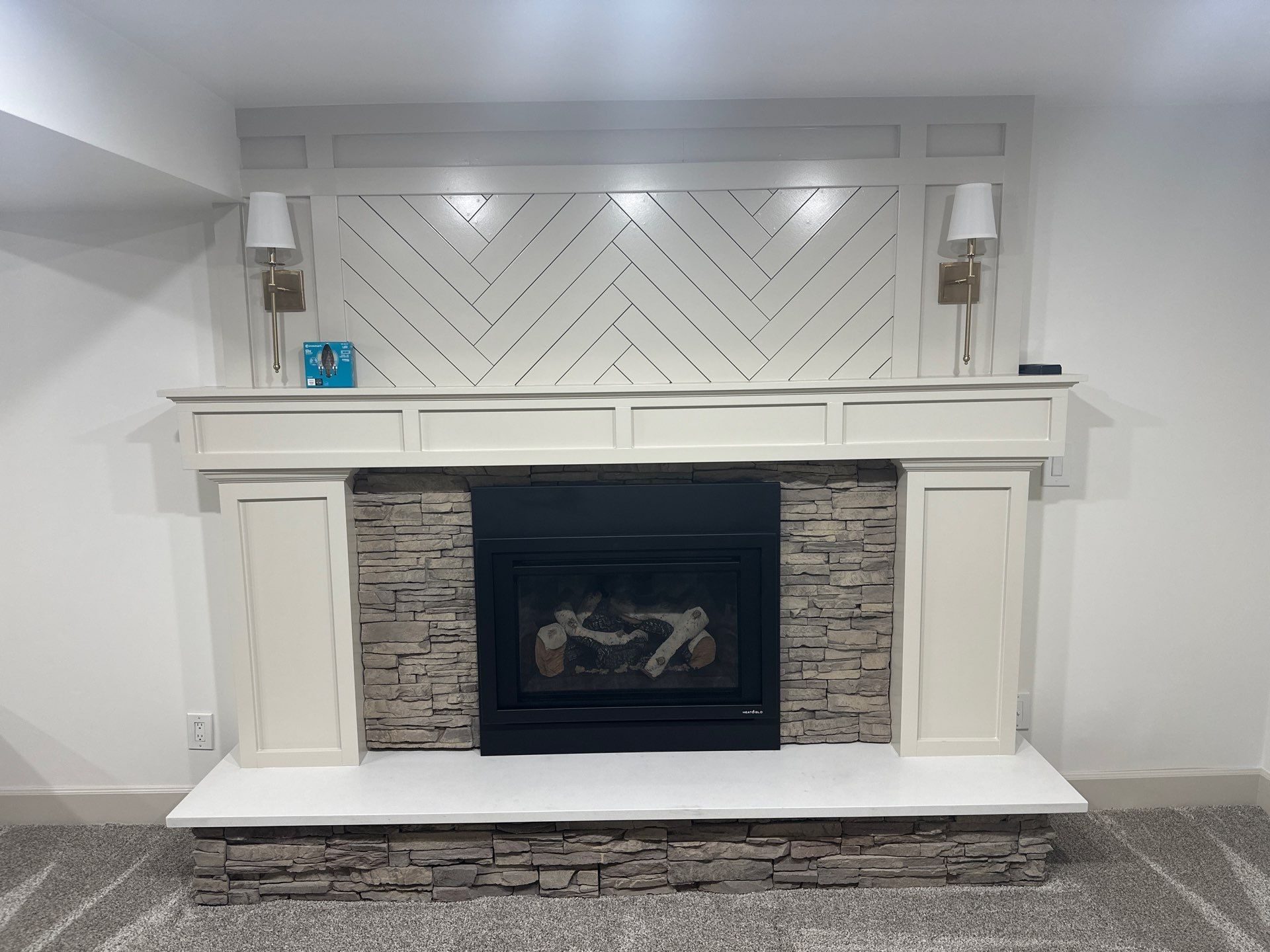 Finished basement fireplace in Cottonwood Heights, Utah with a stacked stone surround, painted mantel and herringbone overmantel