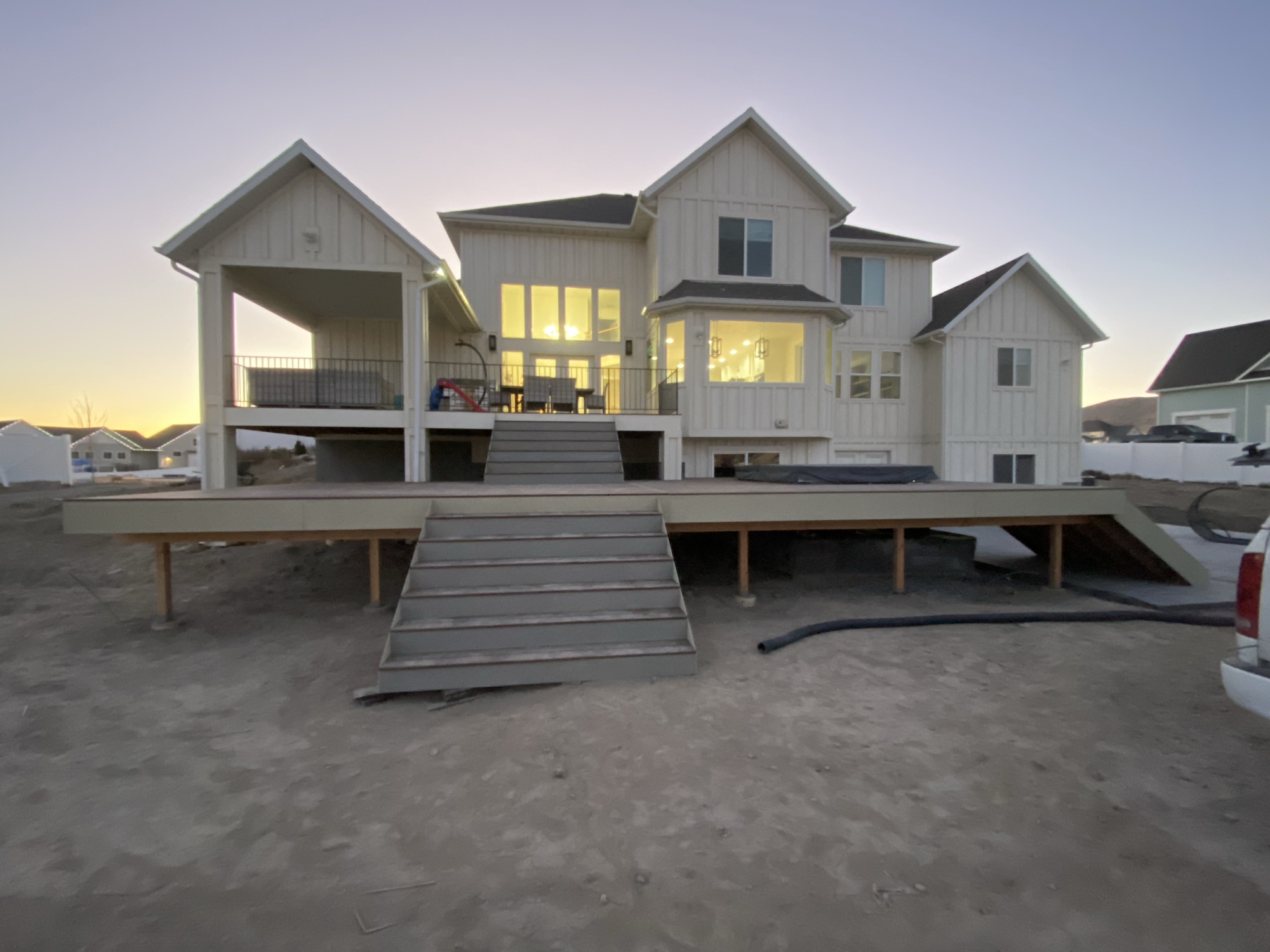 Hillside home addition with a wraparound covered porch at dusk, a Talisman Renovation & Design addition in Herriman, Utah