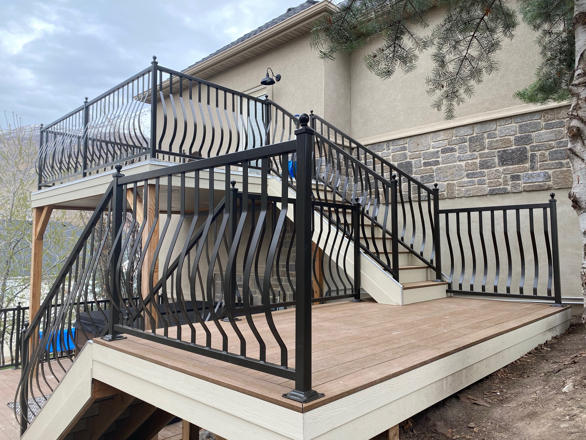 Two-level deck build in Sandy, Utah with custom black wrought-iron ribbon railing and stone veneer columns