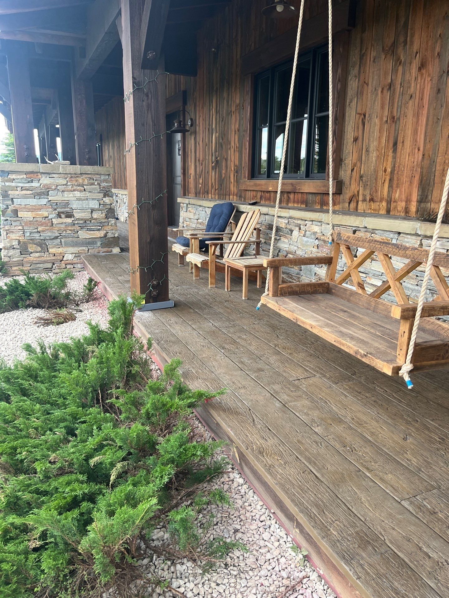 Covered porch with a reclaimed timber swing, dry-stack stone base and wood-textured concrete decking